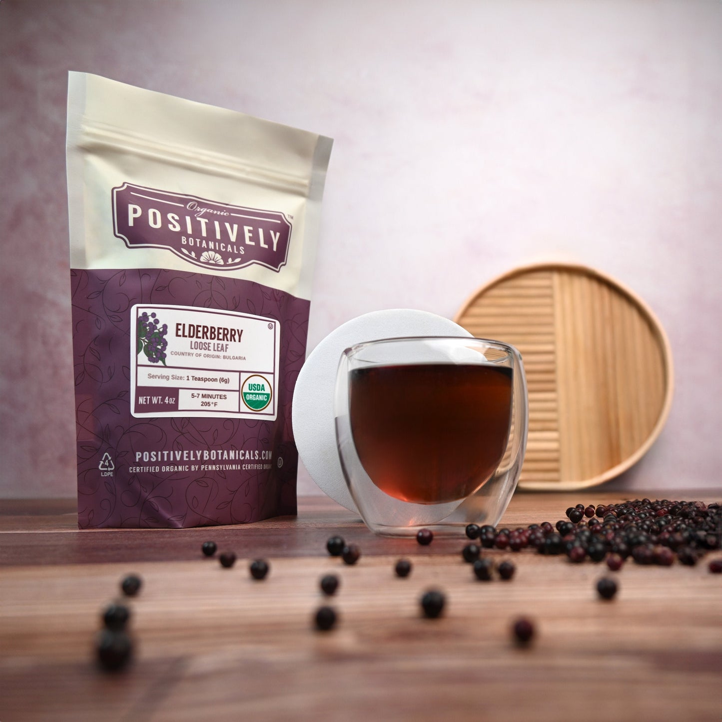 Positively Botanicals Organic Elderberry tea brewed in a glass cup, with loose elderberries and packaging displayed on a wooden surface.