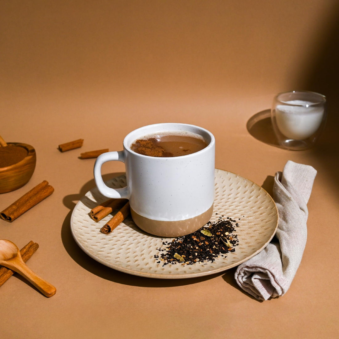 Freshly brewed Masala Chai tea in a ceramic mug, surrounded by cinnamon sticks and spices for a rich, aromatic experience.