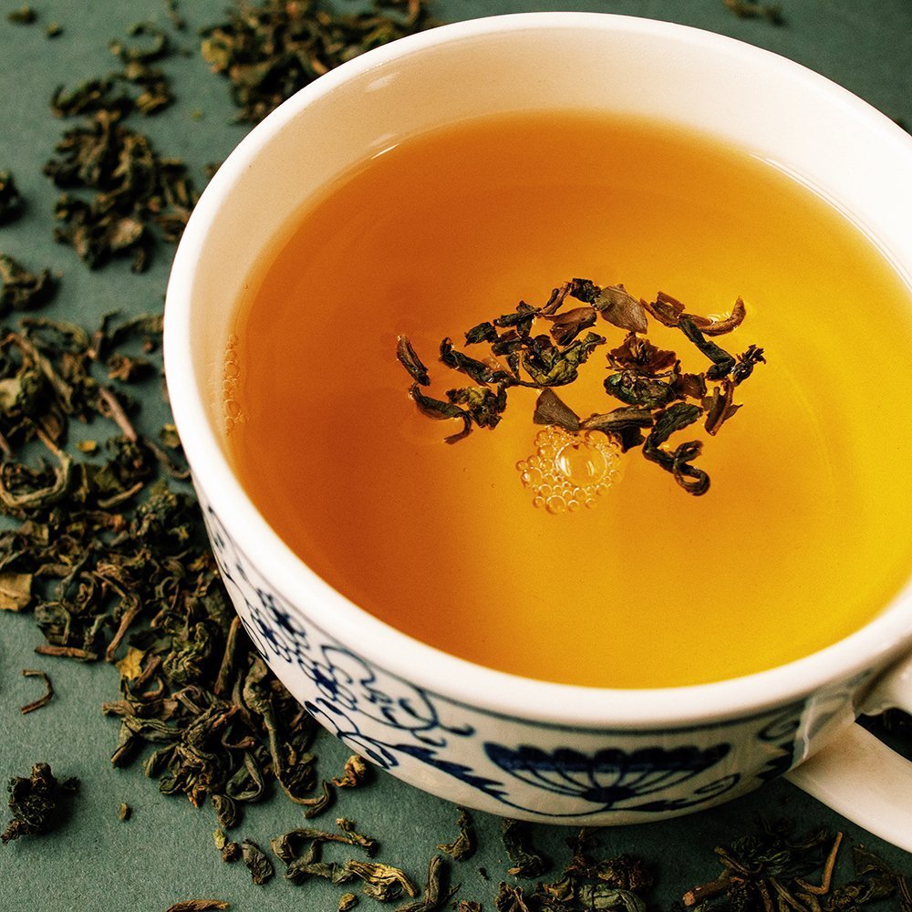 Freshly brewed cup of Jasmine Organic Green Tea with floating tea leaves, highlighting floral aroma and light golden color.