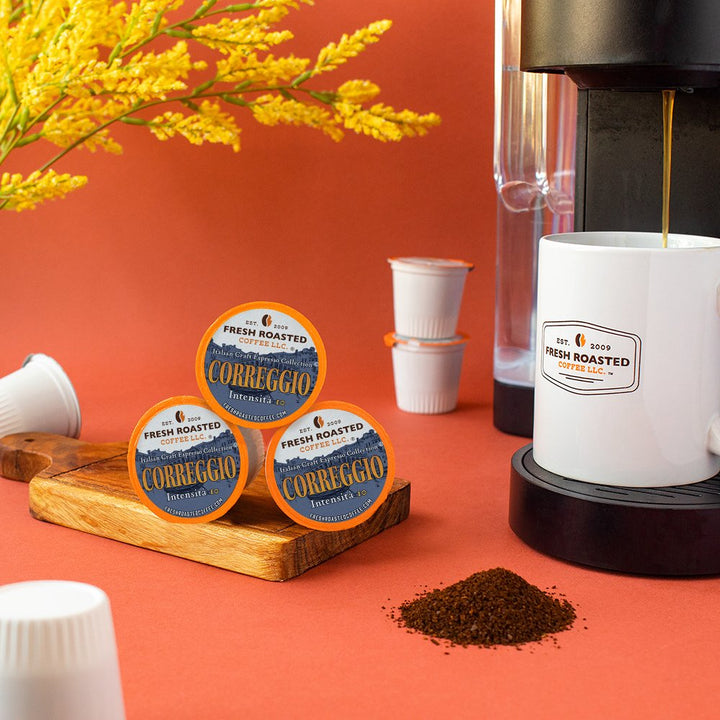 Fresh Roasted Coffee Correggio espresso pods displayed near a coffee maker, with ground coffee and a mug ready for brewing.